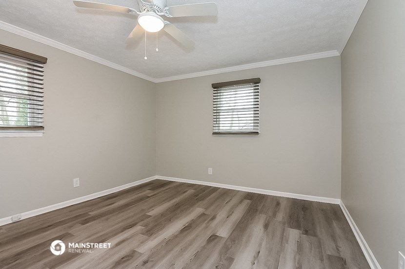 the spacious living room with hardwood flooring and a ceiling fan
