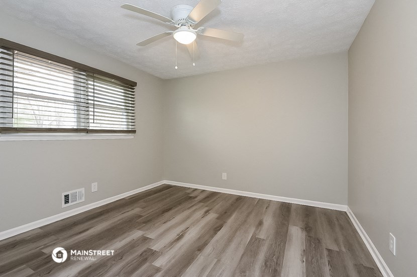the spacious living room with wood flooring and a ceiling fan