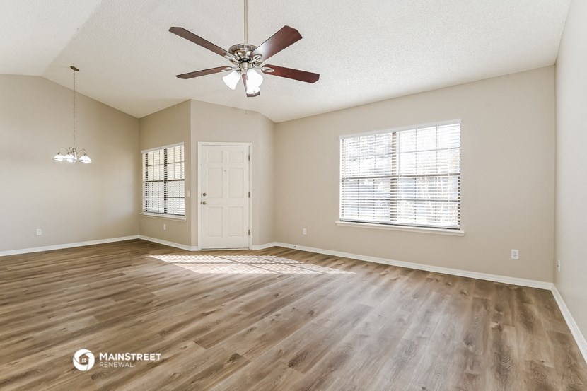 the spacious living room with wood flooring and a ceiling fan
