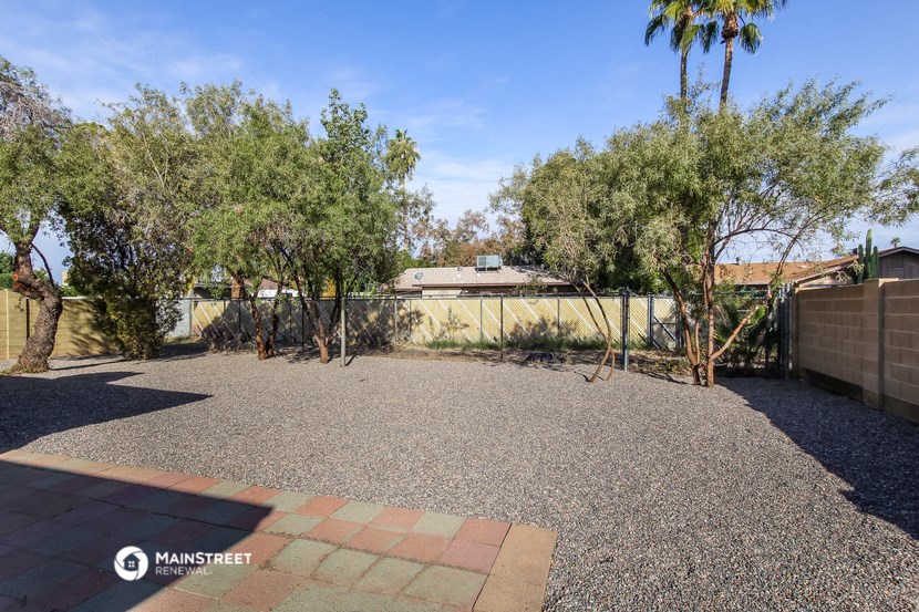 a yard with trees and a fence and a house in the background