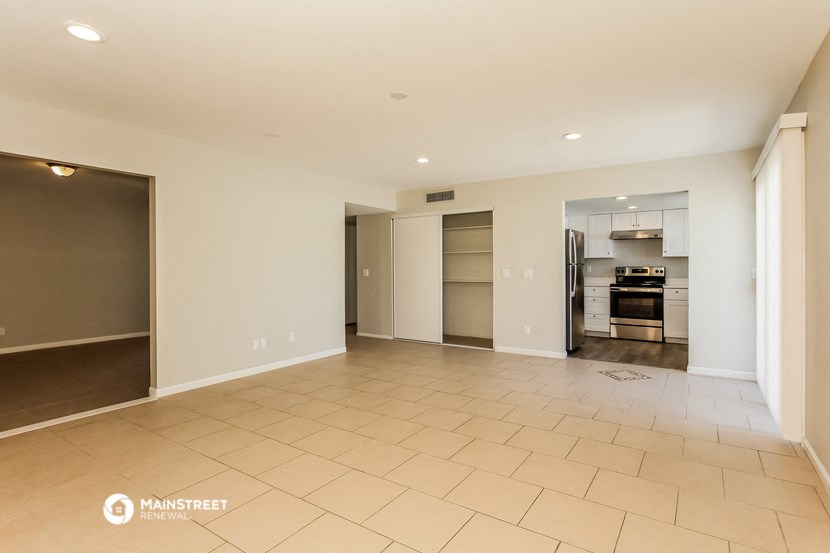 an empty living room with a kitchen in the background