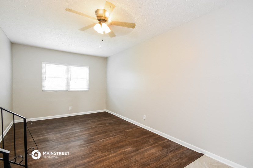 the spacious living room with a ceiling fan and wood flooring