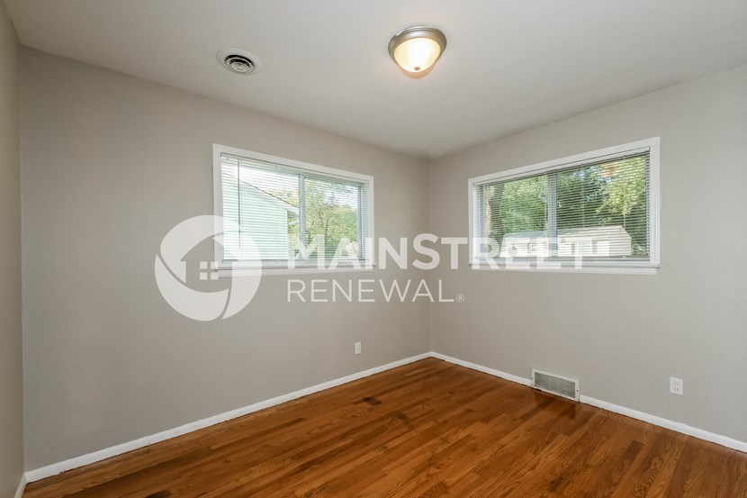 a bedroom with a wood floor and two windows