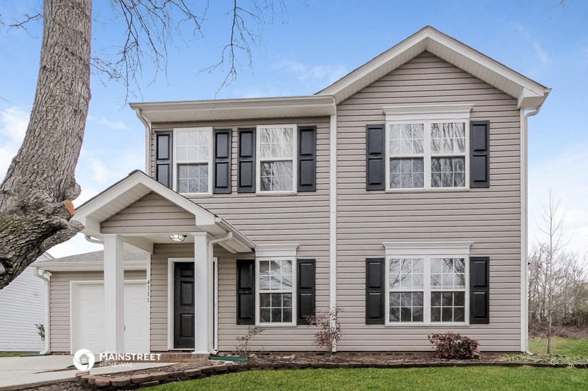 a beige house with black shutters and a tree