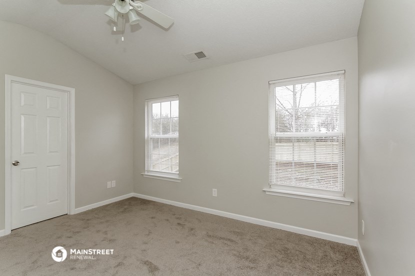 the spacious living room with two windows and a ceiling fan