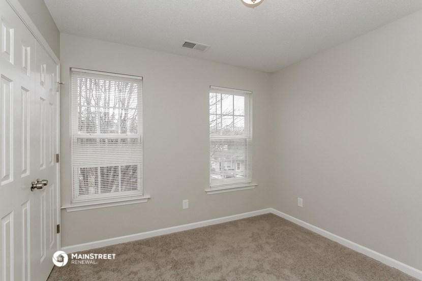 the spacious living room of this manufactured home has a carpeted floor and two windows