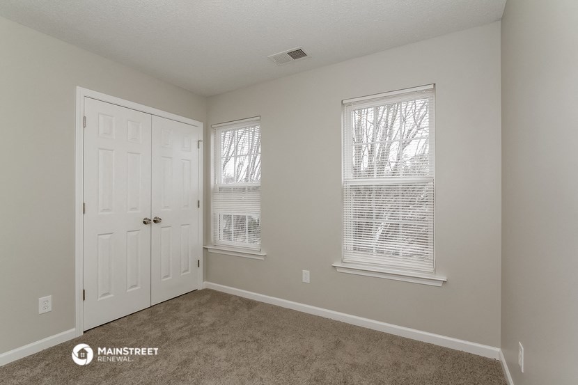 a bedroom with carpet and a door and two windows