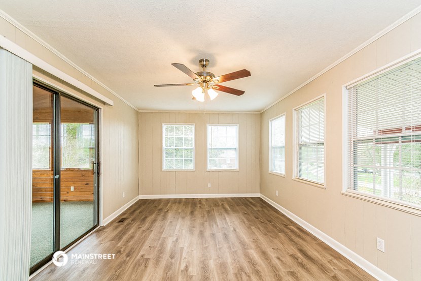 an empty living room with a ceiling fan and windows