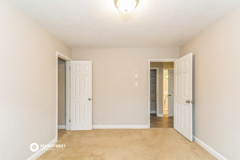 an empty living room with two doors and a hallway to two closets