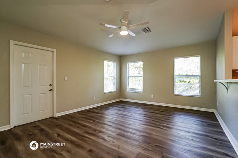 an empty living room with a white door and a ceiling fan