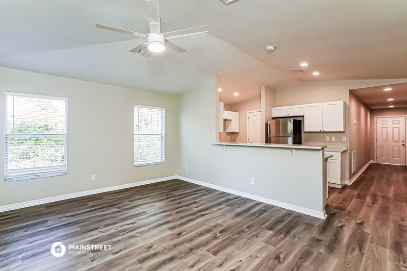 an empty living room with a kitchen and a ceiling fan