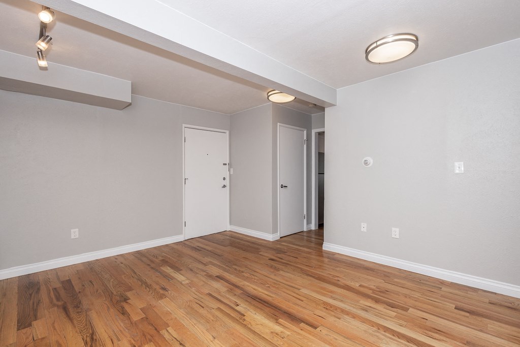 the living room of an apartment with wood flooring and white walls
