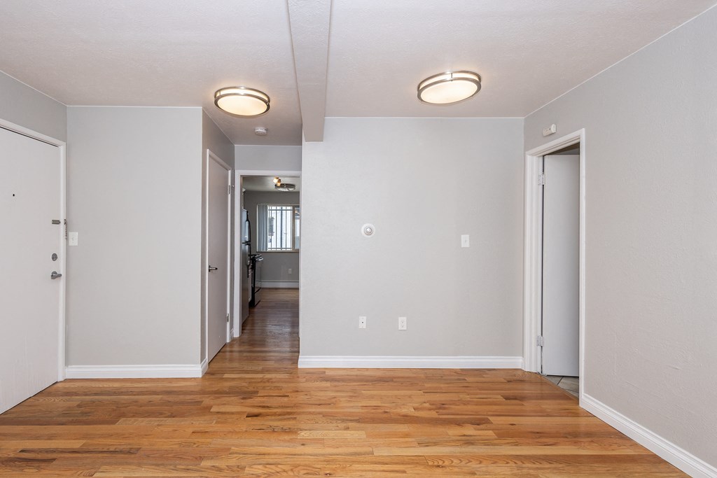 the living room and hallway of an apartment with wood flooring and white walls