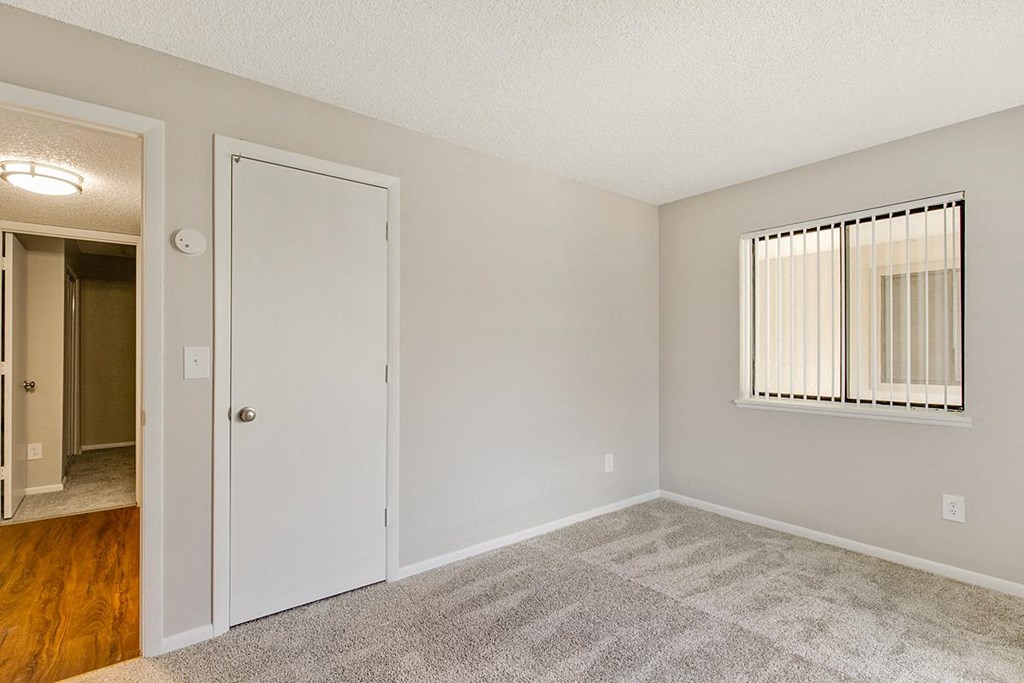an empty bedroom with a door to a hallway and a window