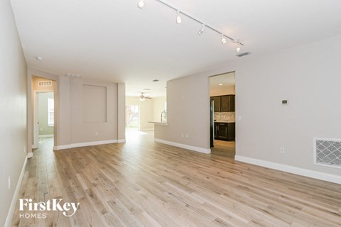 A spacious room with wooden flooring and white walls, with a door on the left and a window on the right.
