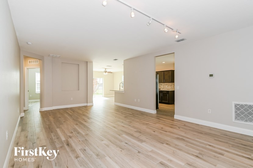 A spacious room with wooden flooring and white walls, with a door on the left and a window on the right.