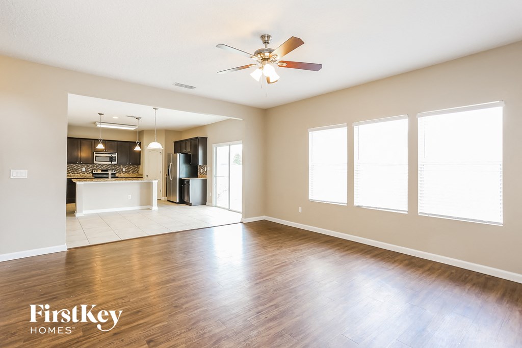 an empty living room with a ceiling fan and a kitchen