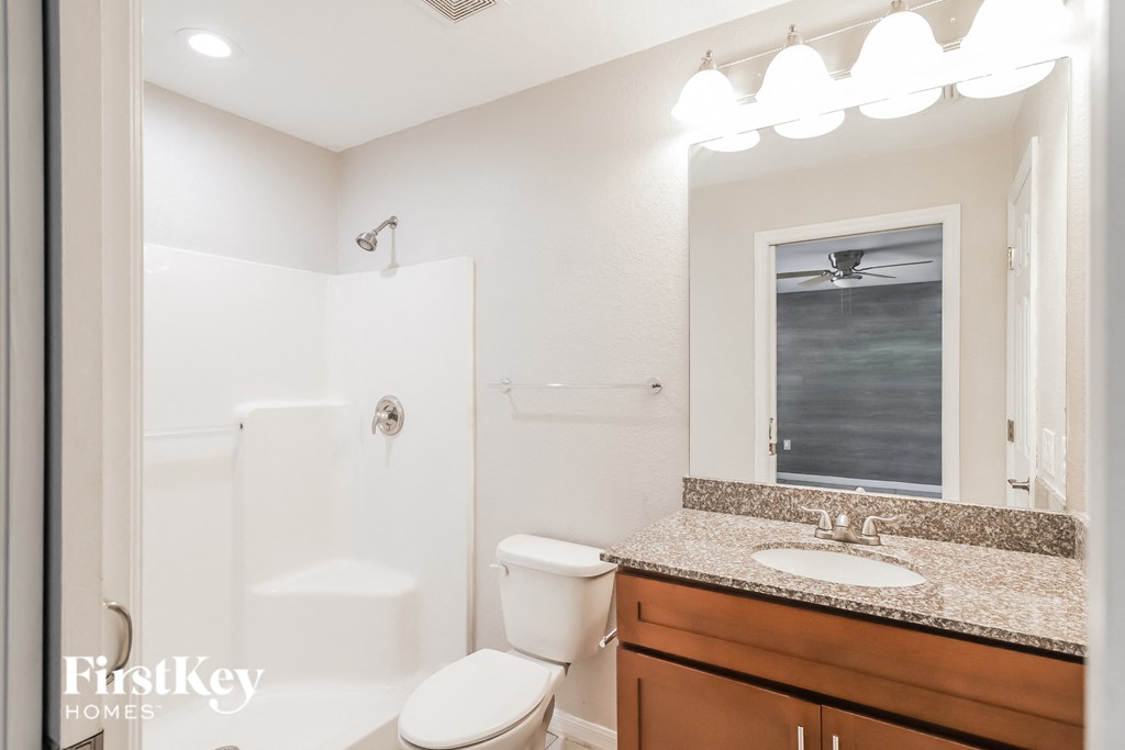 A white toilet sits in a bathroom with a wooden vanity and a mirror.