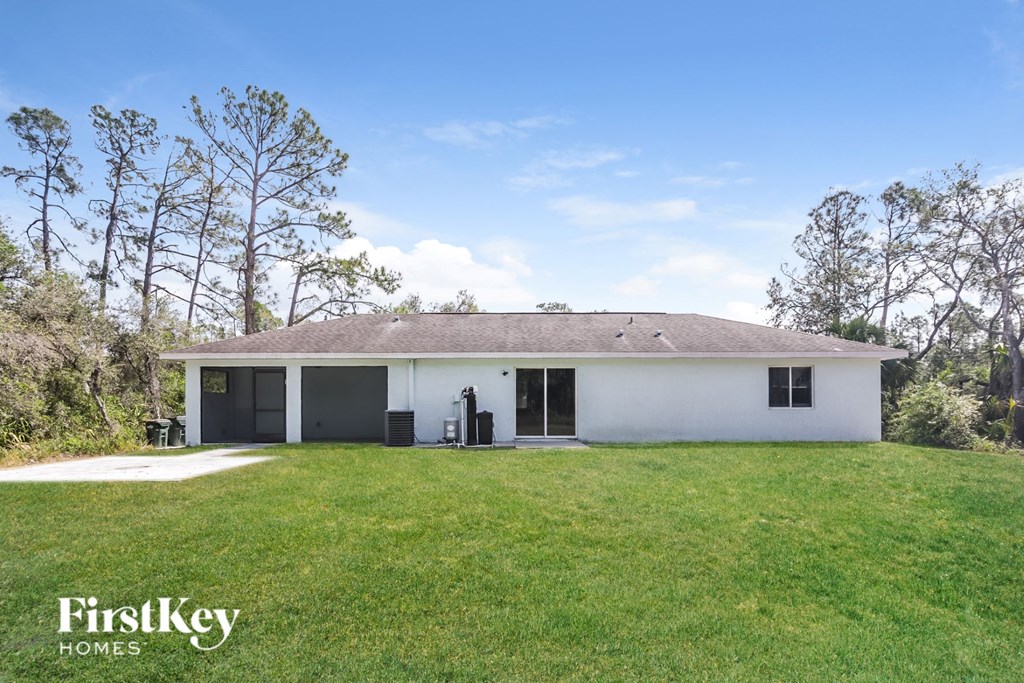A white house with a black door and windows is surrounded by green grass and trees.