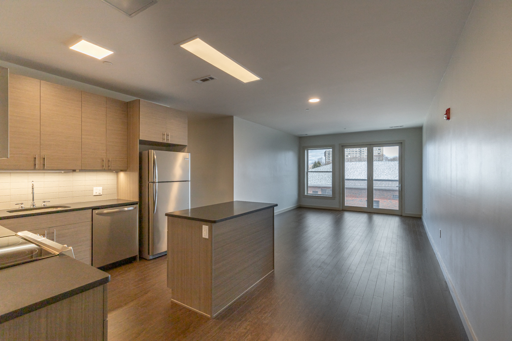 an empty kitchen with wood flooring and a stainless steel refrigerator