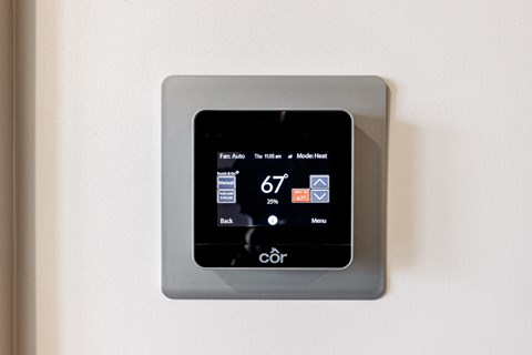 a smart thermostat on a white wall with a digital screen on it