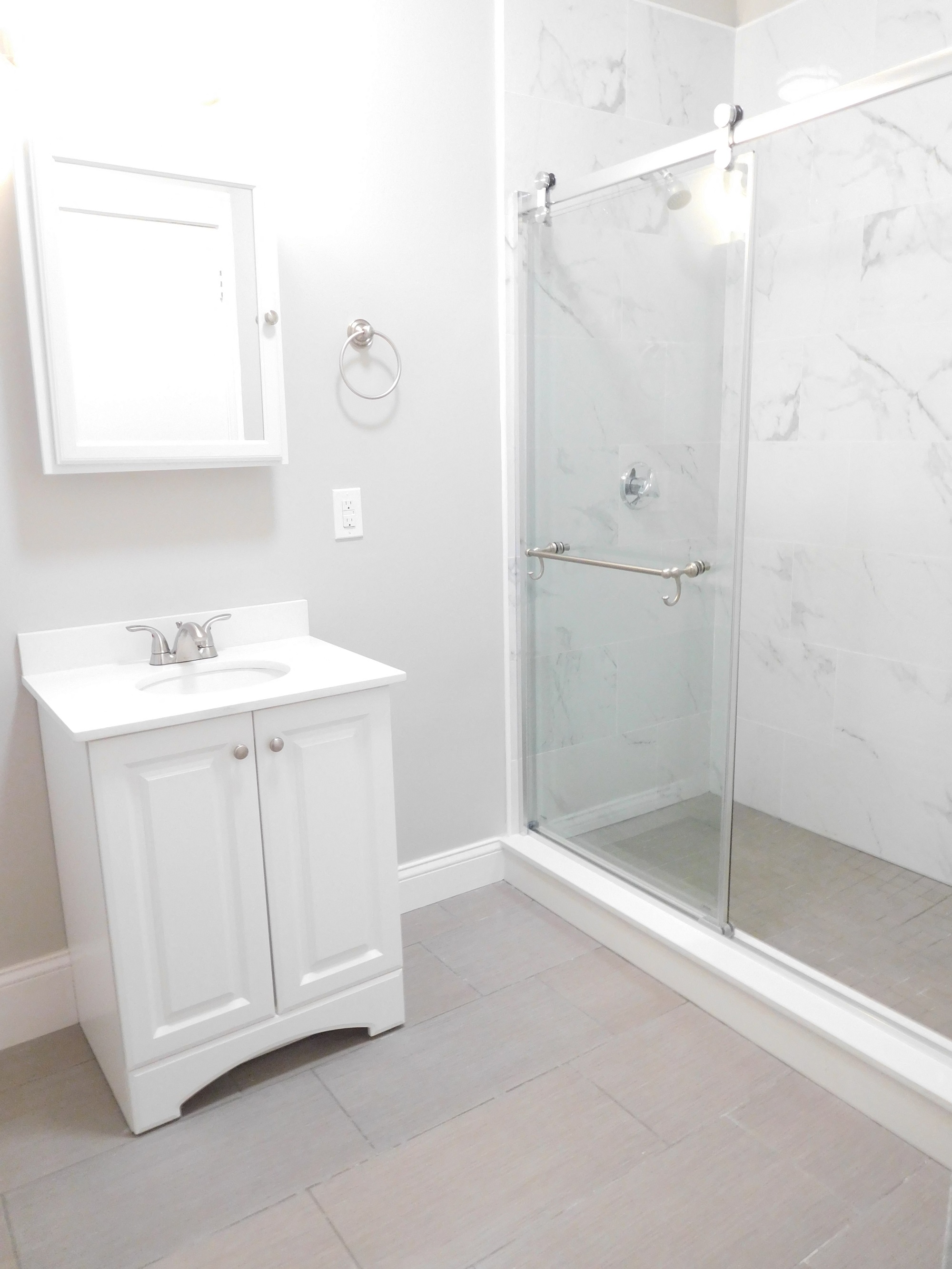 Renovated Bathroom with Gray Tile Floors, White Vanity and Glass Shower Stall