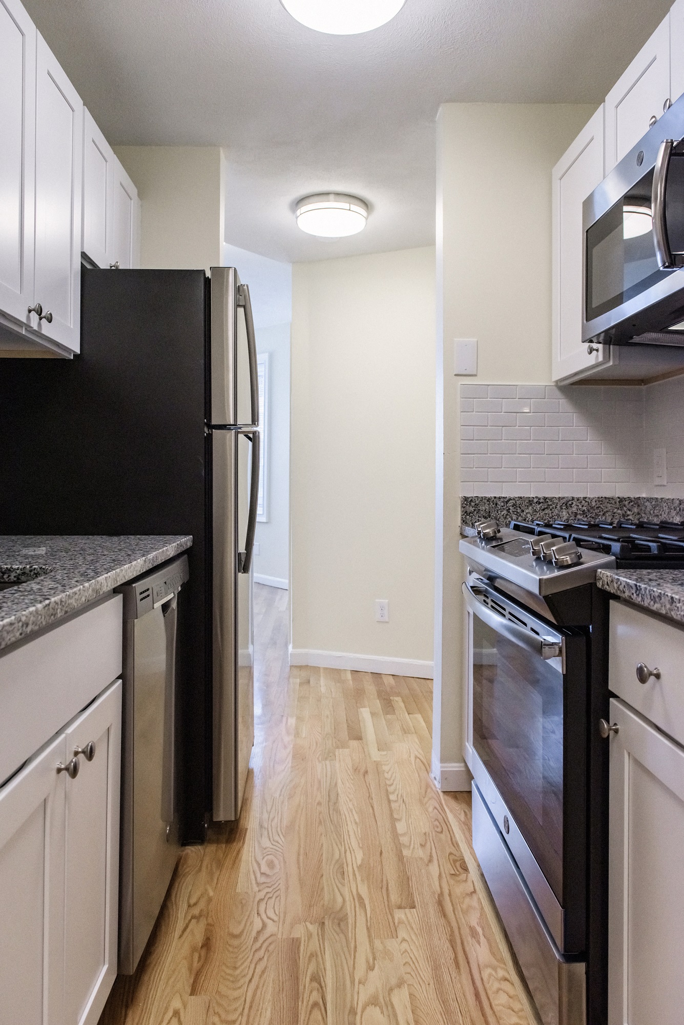 Galley Kitchen with White Cabinets, Stainless Appliances, Gas Stove, Granite Counters, White Subway Tiles, Hardwood Floors