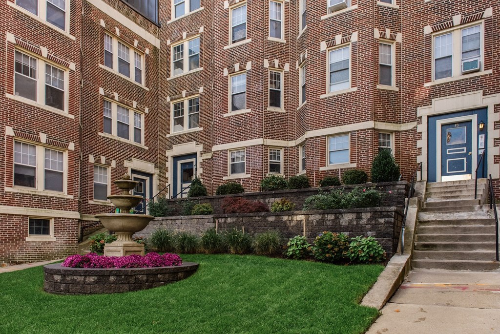 the front of a brick building with a fountain in the yard