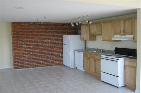 a kitchen with white appliances and a brick wall