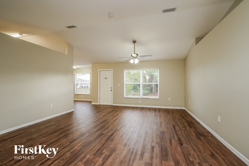the spacious living room with hardwood flooring and a ceiling fan