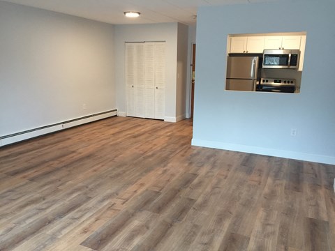 an empty living room with wood flooring and a refrigerator