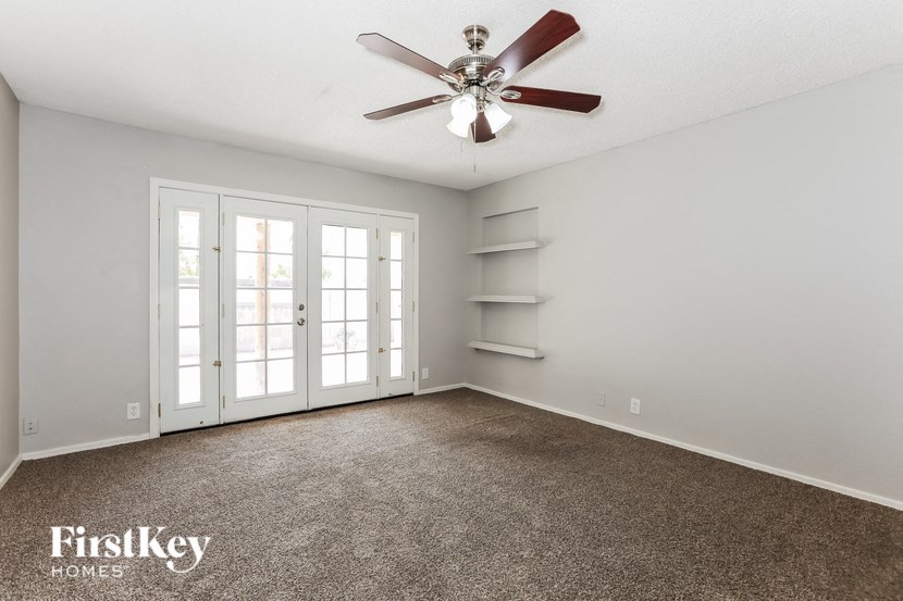 an empty living room with a ceiling fan and white shelves