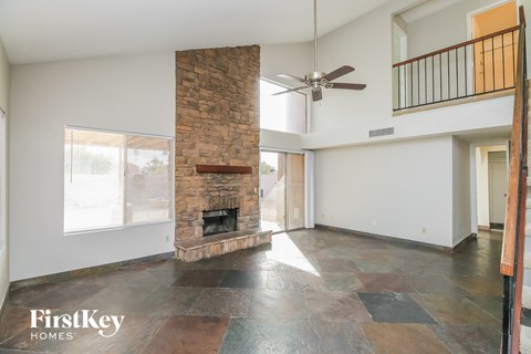 A spacious living room with a stone fireplace and a fan.