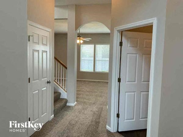 A hallway with a carpeted floor, a staircase with a railing, and a door on the right.