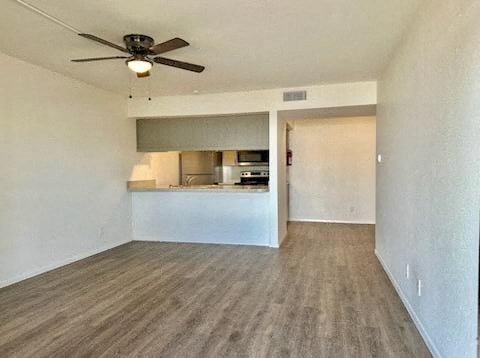 an empty living room with a ceiling fan and a kitchen