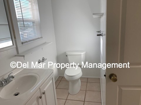 A white toilet in a small bathroom with a sink and a window.