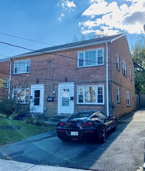 A black sports car is parked in front of a red brick house.