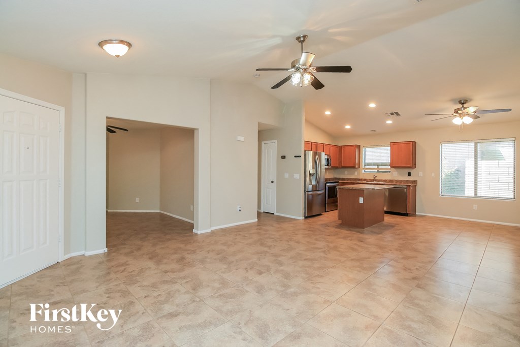 A spacious room with a ceiling fan and a kitchen area in the background.