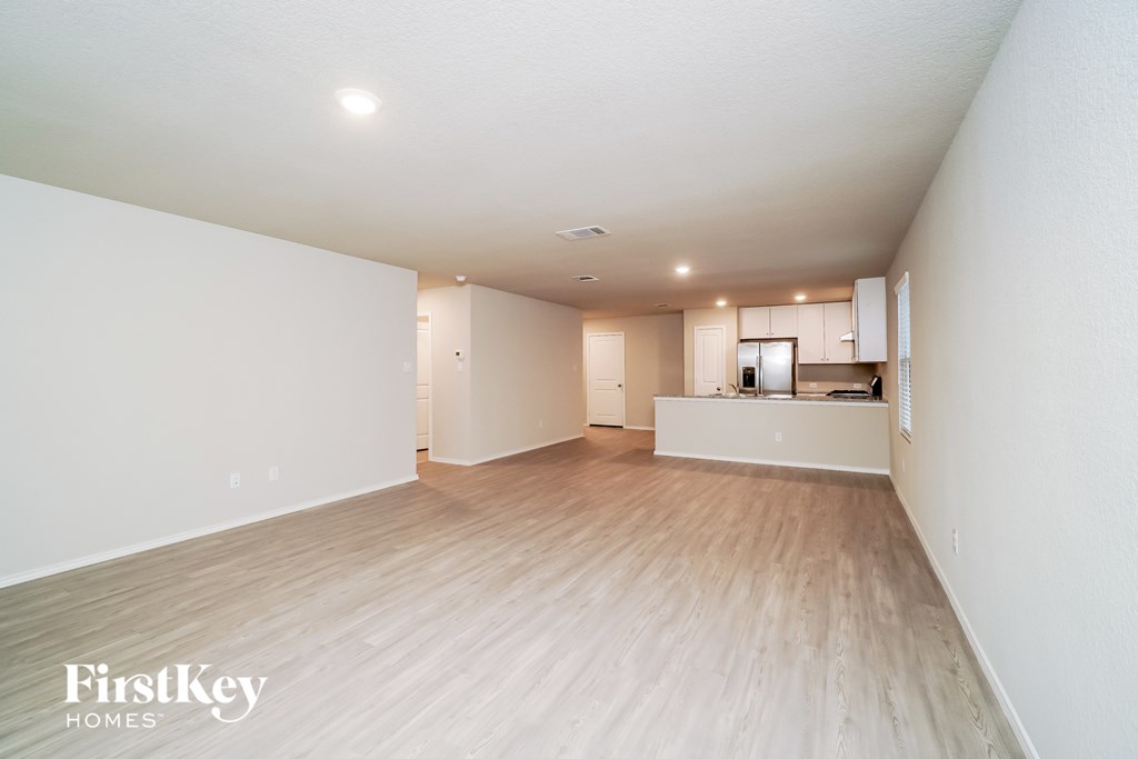 a spacious living room and kitchen with white walls and wood flooring