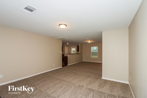 a spacious living room with carpet and a kitchen