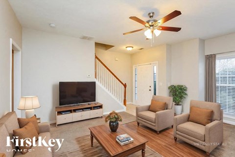 A living room with a television, two chairs, a coffee table, and a ceiling fan.