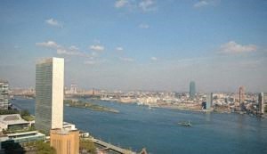 A cityscape with a large body of water in the foreground and a tall white building in the background.
