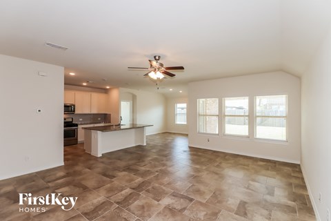 A spacious living room with a kitchen in the background and a tiled floor.
