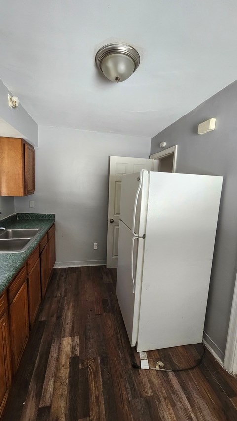 A white refrigerator stands in a kitchen with wooden floors and a green counter.