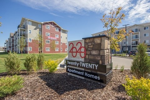A sign for Twenty-Twenty Apartment Homes stands in front of a building.