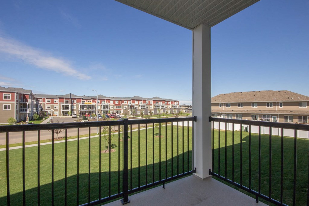A balcony overlooks a green field and apartment buildings.