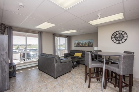 A living room with a grey couch, a table and a clock on the wall.
