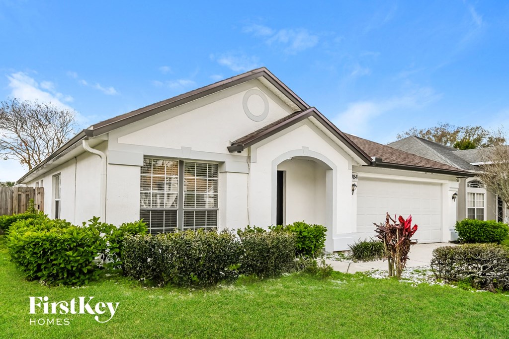 the front of a white house with a lawn and shrubs