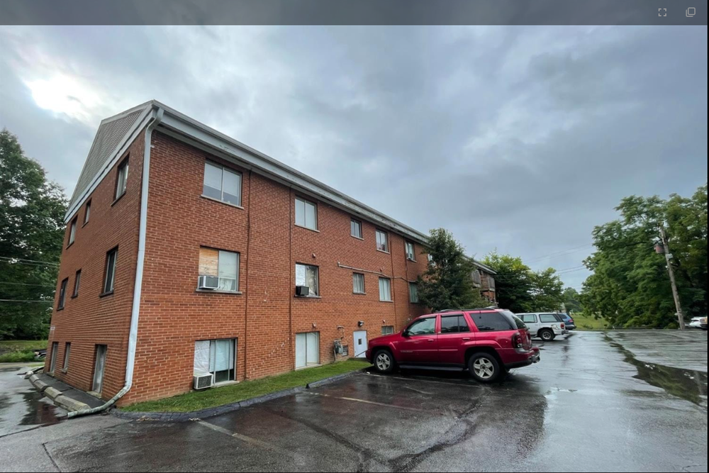 A red car is parked in front of a brick building on a cloudy day.