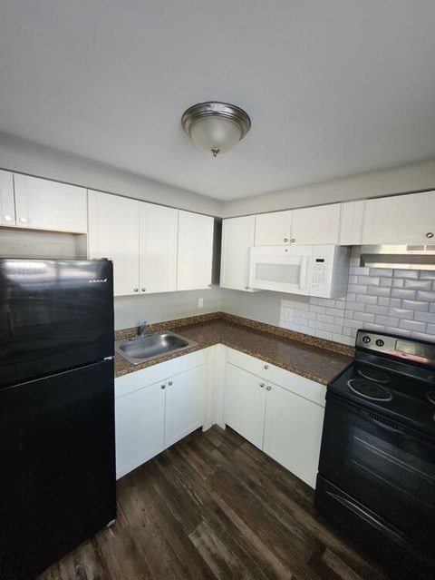 A black fridge and oven in a kitchen with white cabinets.